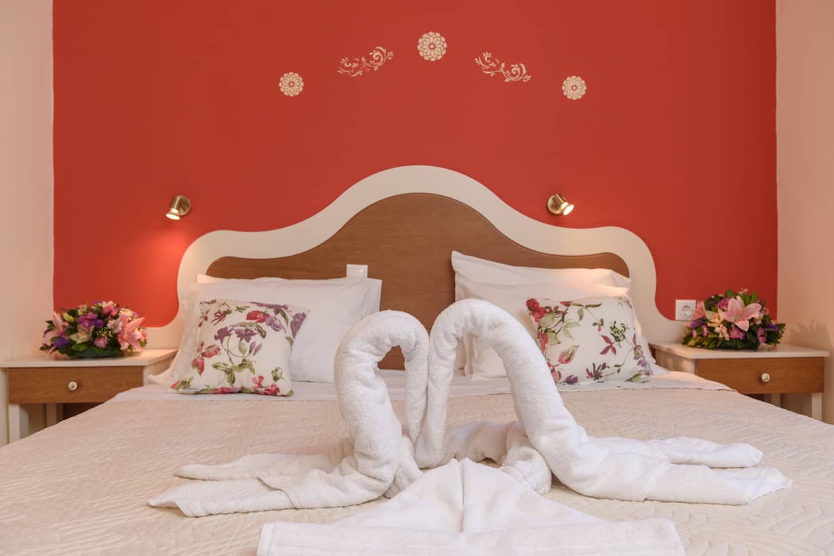 A neatly made bed with two towels arranged in a heart shape, a floral pillow, and a wall with decorative floral stickers.