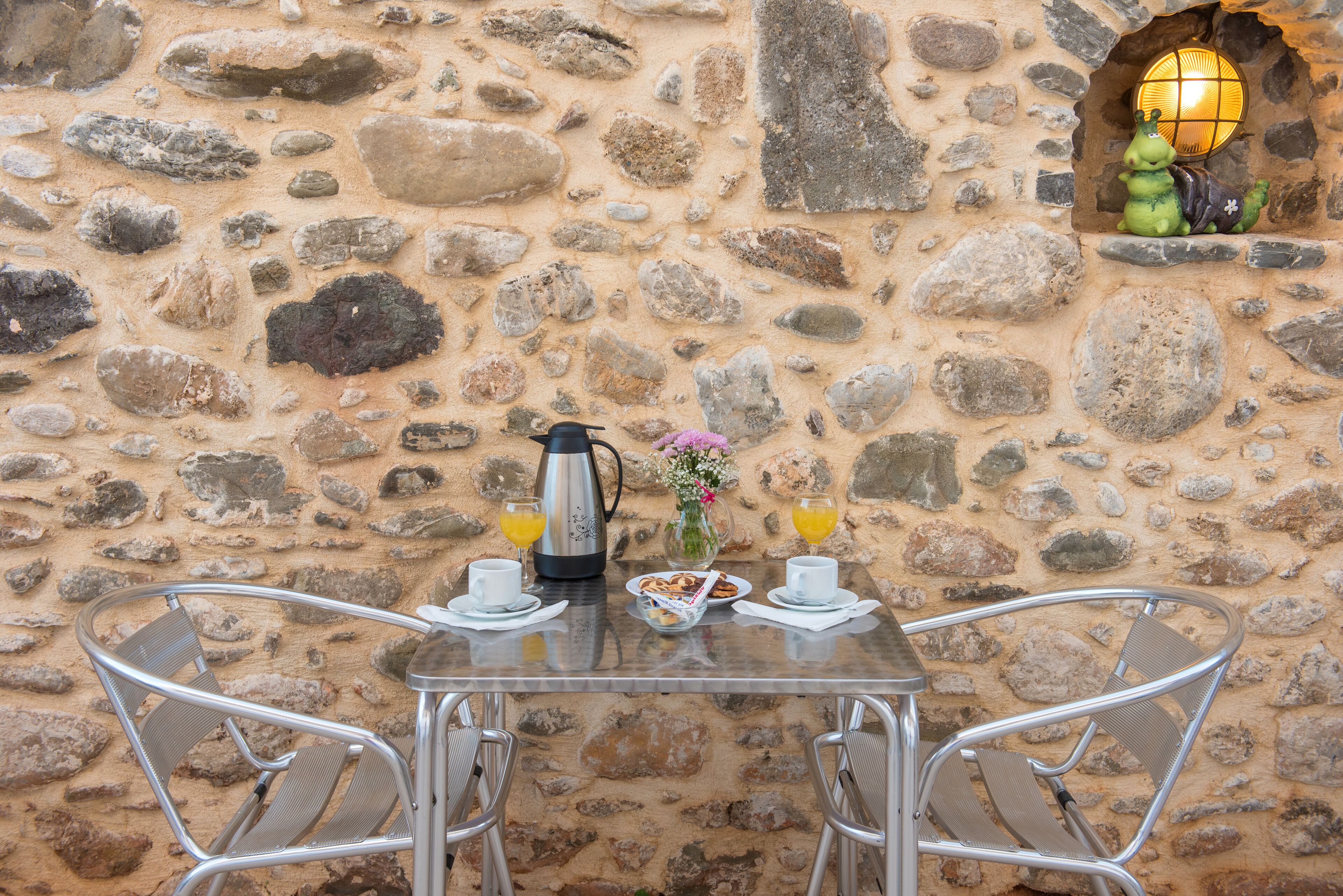A stone wall with a table set for two, including a coffee pot, cups, and a plate of food.
