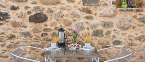 A stone wall with a table set for two, including a coffee pot, cups, and a plate of food.