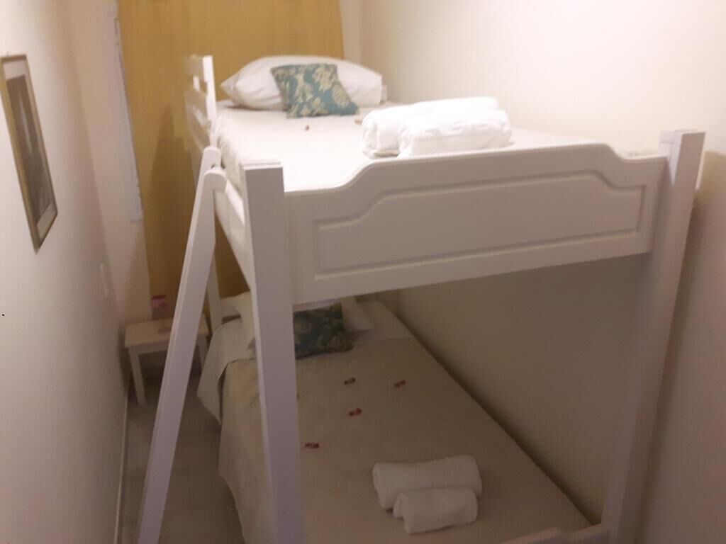 A bunk bed with white bedding and a small table with a pillow.