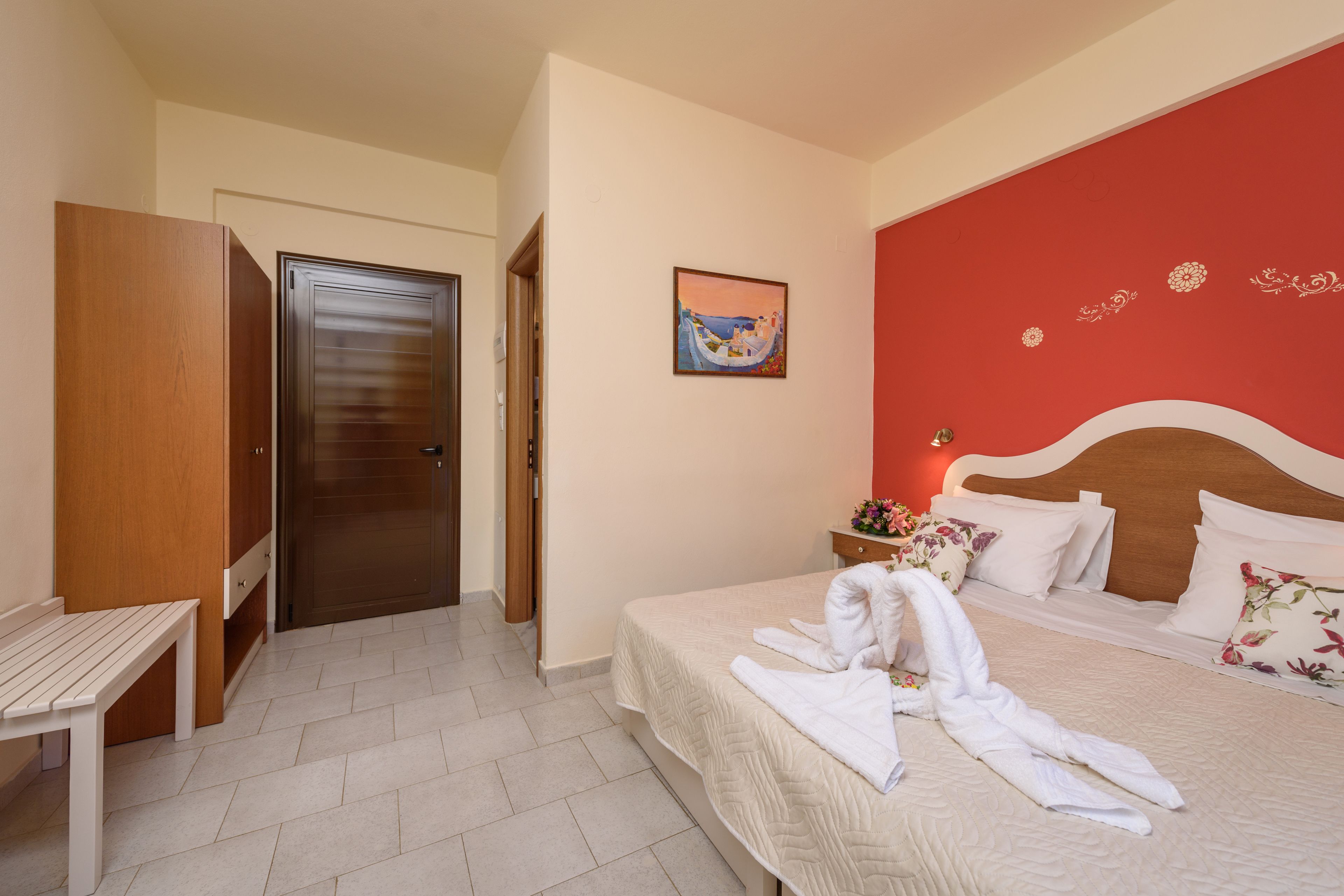 Una habitación de hotel con una cama, un armario de madera, un banco y una puerta.