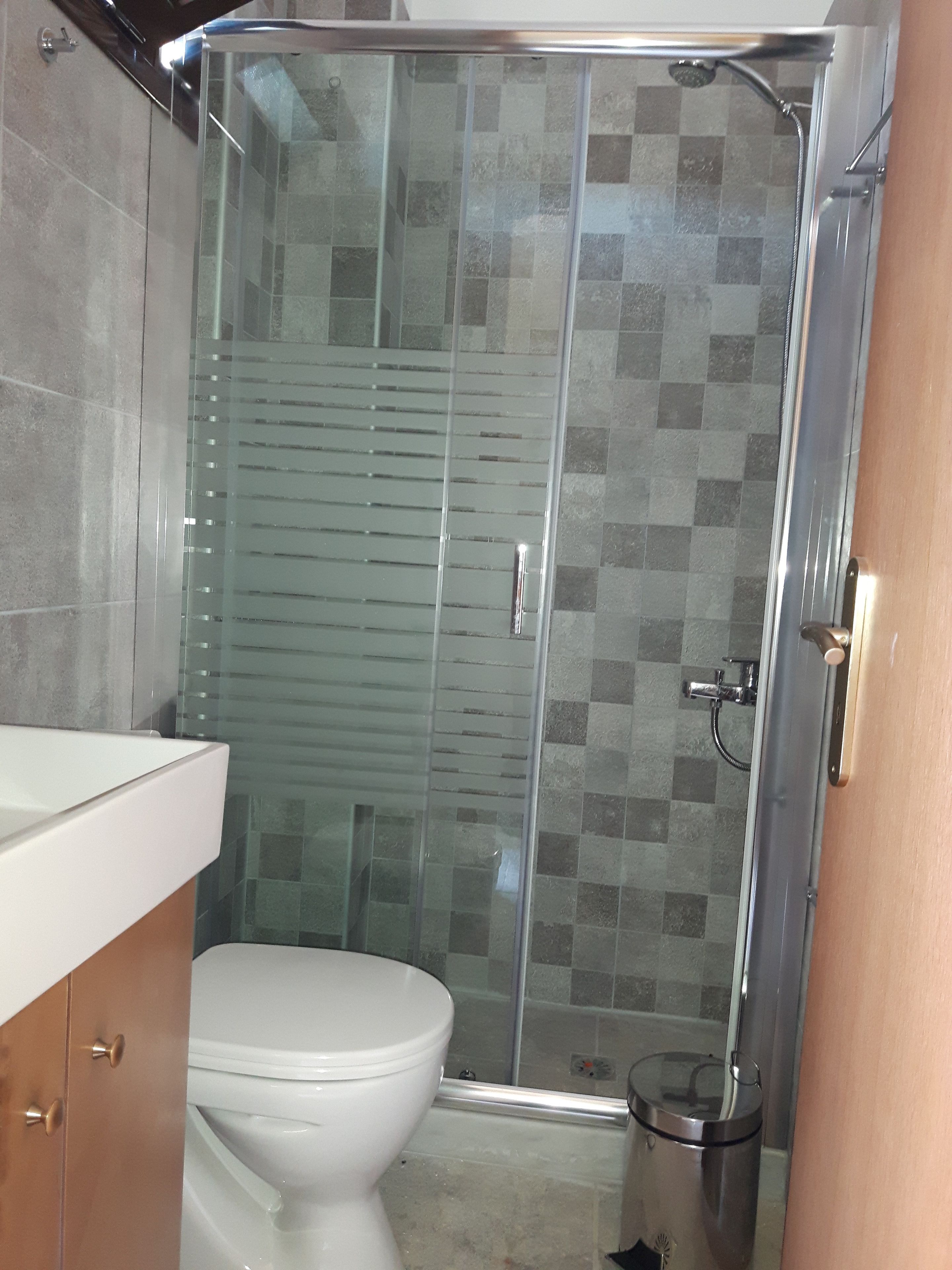 Baño con cabina de ducha de vidrio, inodoro y cubo de basura.