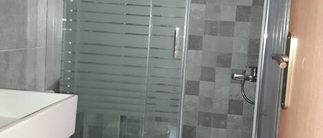 Baño con cabina de ducha de vidrio, inodoro y cubo de basura.