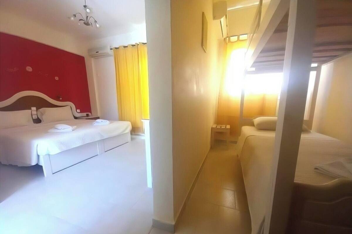 A hotel room with a bed, a sofa, a bedside table, a lamp, and a window with curtains.