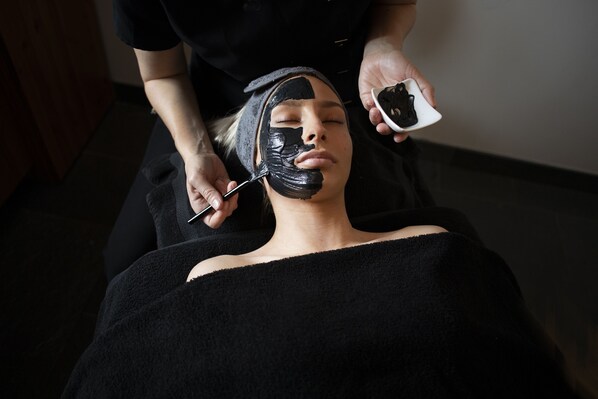 A person receiving a facial treatment with a black mask.
