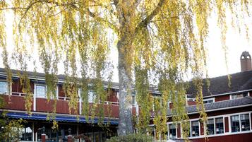 Un edificio tradicional de dos pisos con fachada roja y detalles blancos, con un gran árbol de hojas amarillas al frente.