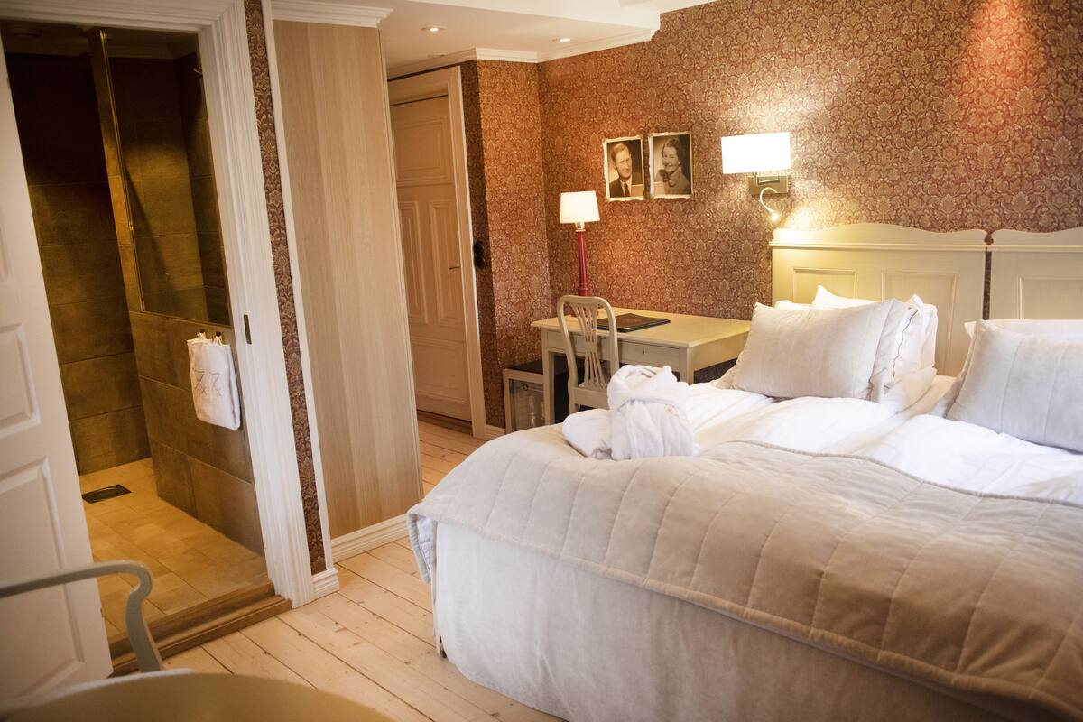 Ein Hotelzimmer mit Bett, Schreibtisch, Stuhl, Lampe und einer Duschkabine.