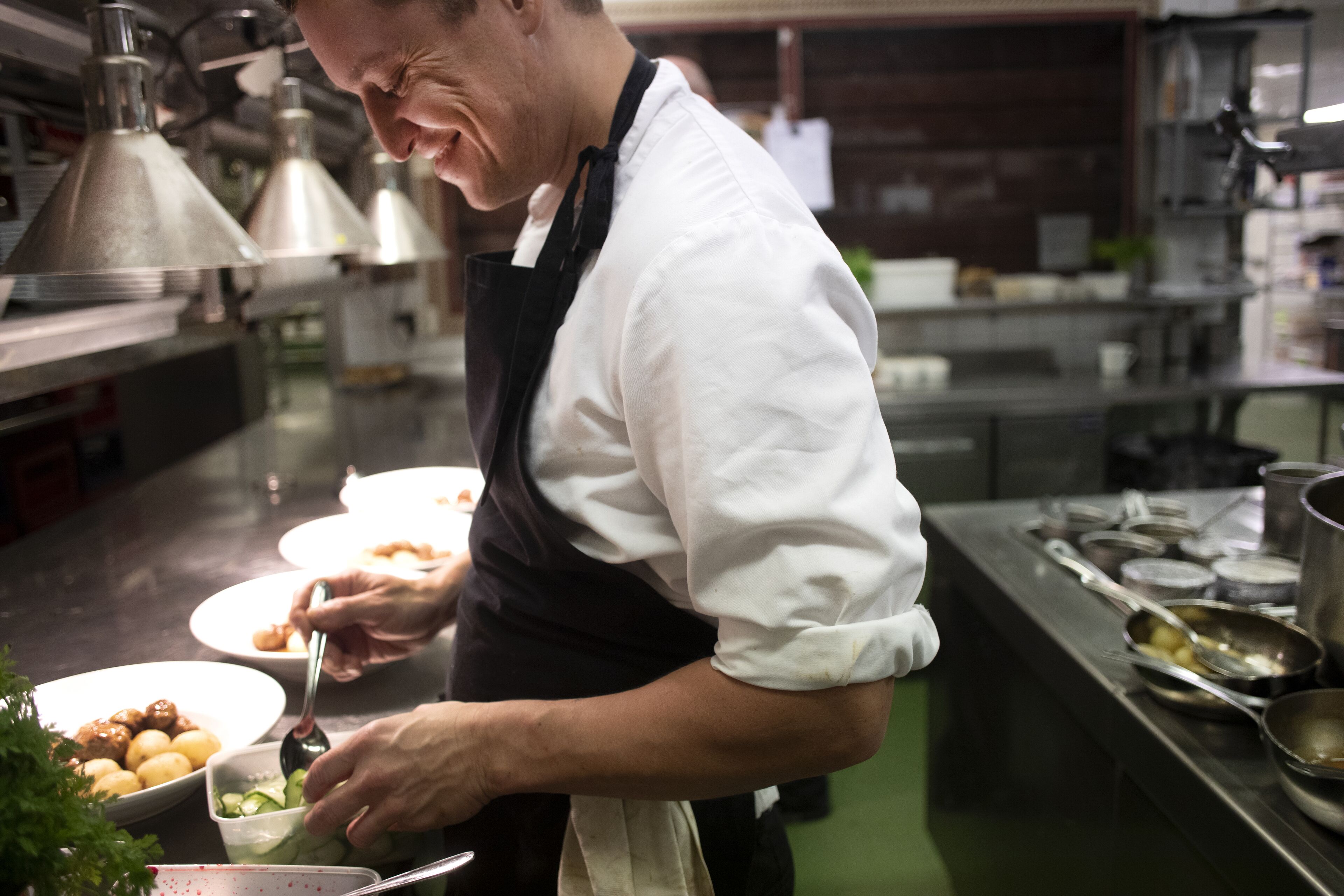 Um chef em uma cozinha profissional com eletrodomésticos de aço inoxidável e chão verde.