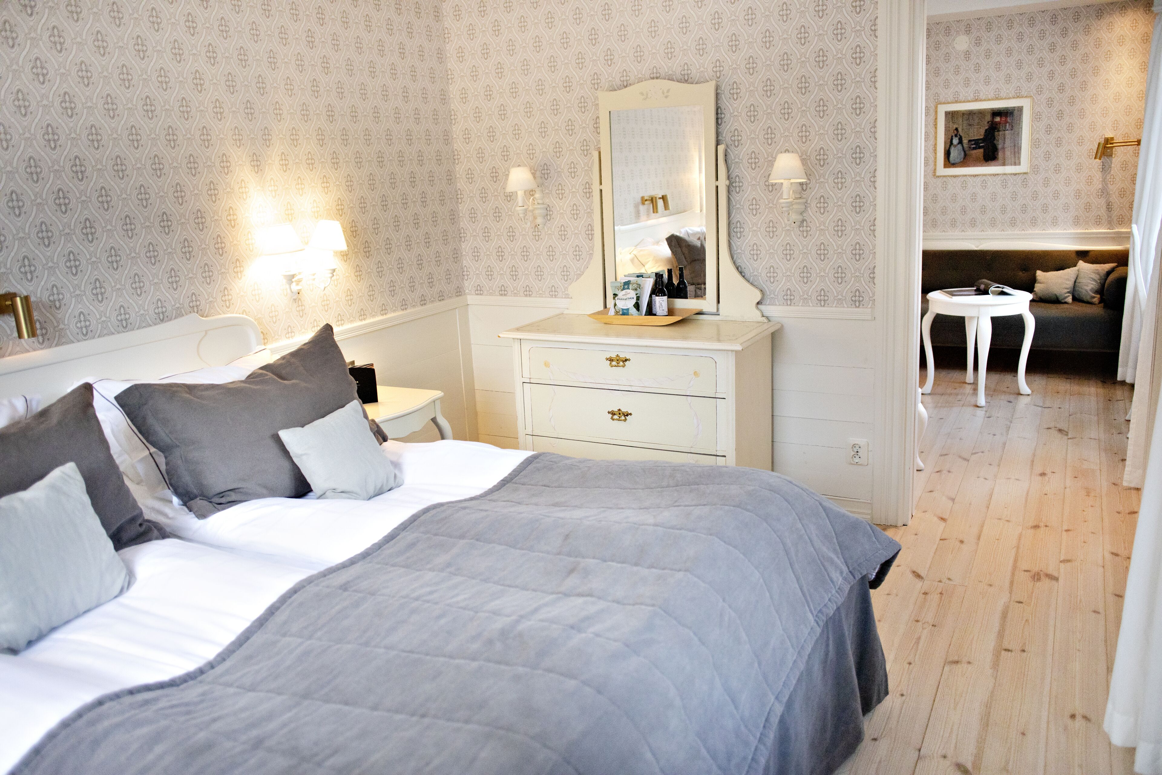 A neatly arranged bedroom with a large bed, bedside tables, a dresser, and a mirror.