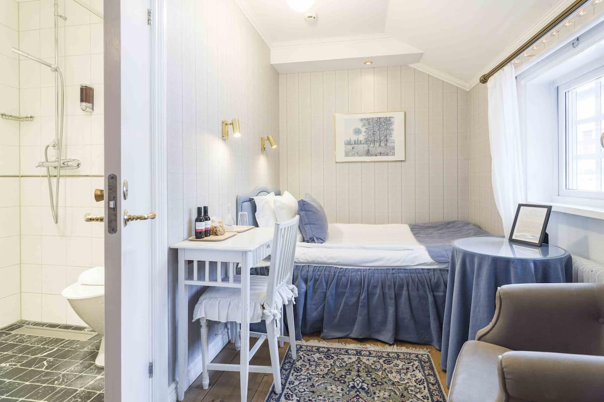 Ein Schlafzimmer mit Bett, Schreibtisch, Stuhl, kleinem Tisch, Fenster und einer Dusche.