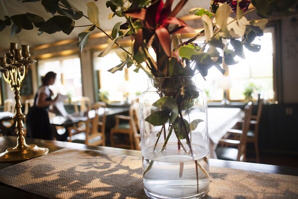 A clear glass vase with water and flowers on a table in a dining area. - Åkerblads Gästgiveri Hotell Spa (Tallberg)