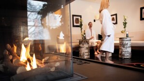 A modern interior with a glass fireplace, a sofa, and a mirror reflecting a person in a robe. - Åkerblads Gästgiveri Hotell Spa (Tallberg)