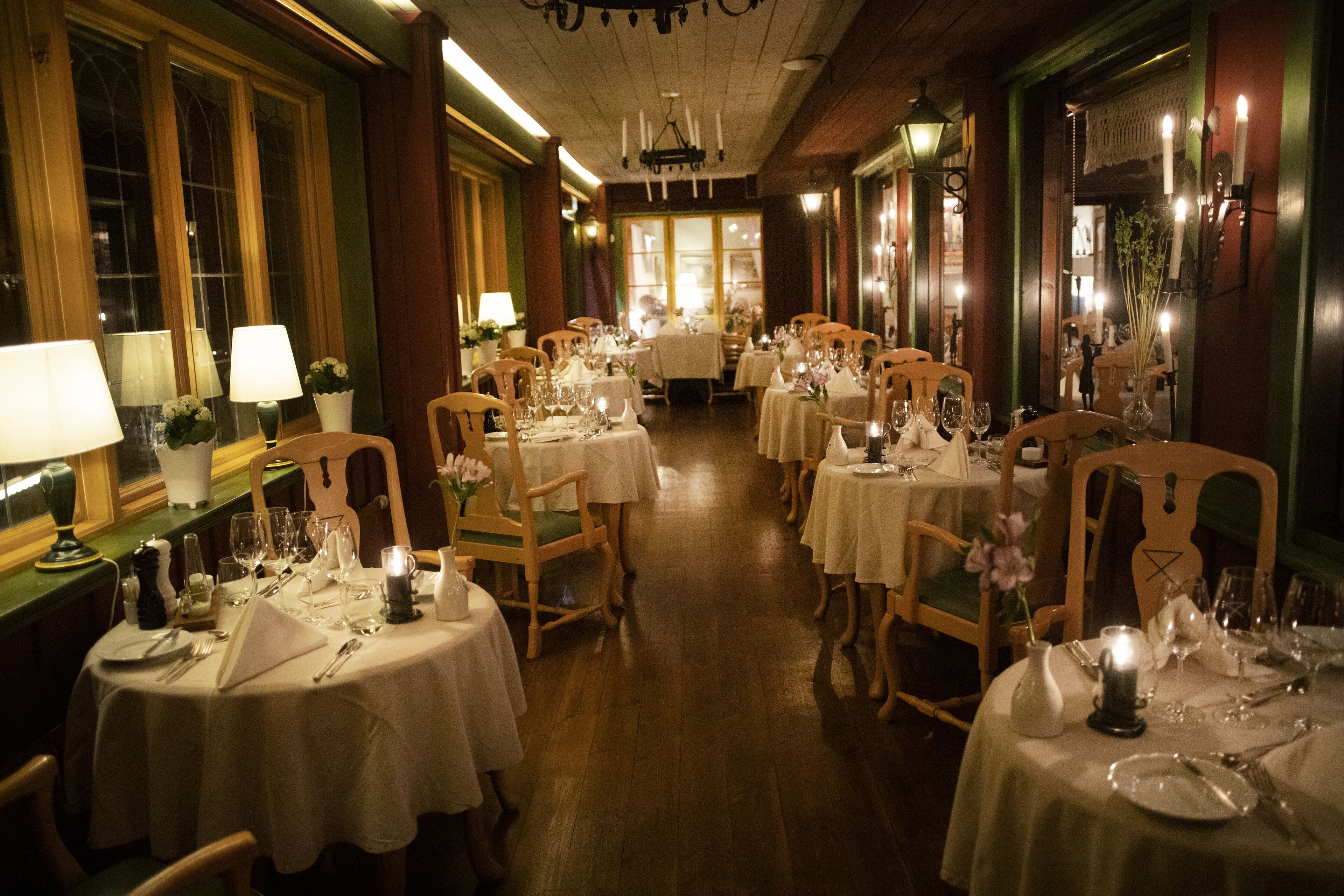 Un restaurante con varias mesas redondas dispuestas para comer, cada una con mantel blanco y velas.