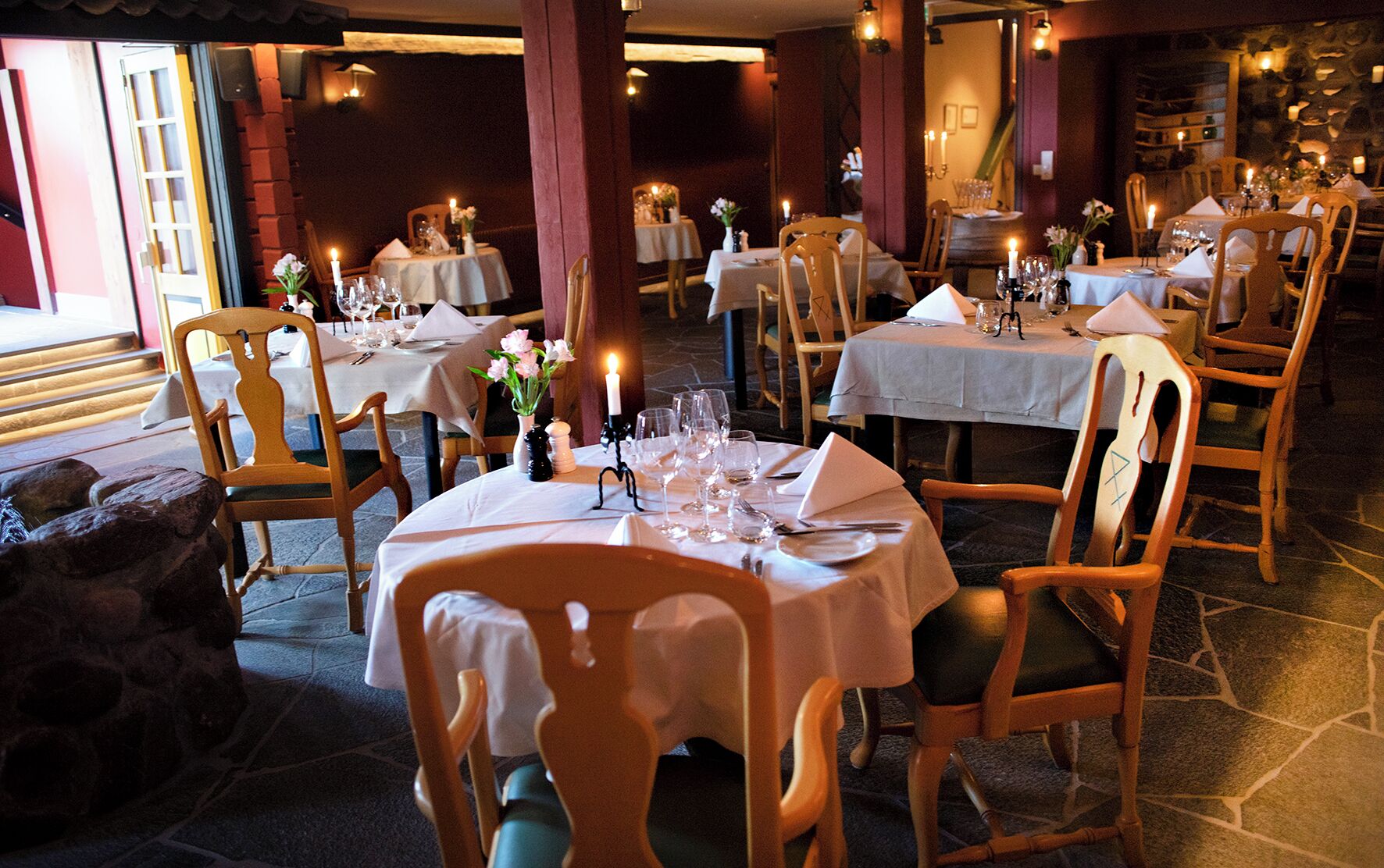 A restaurant with multiple tables set for dining, each with chairs, candles, and table settings.