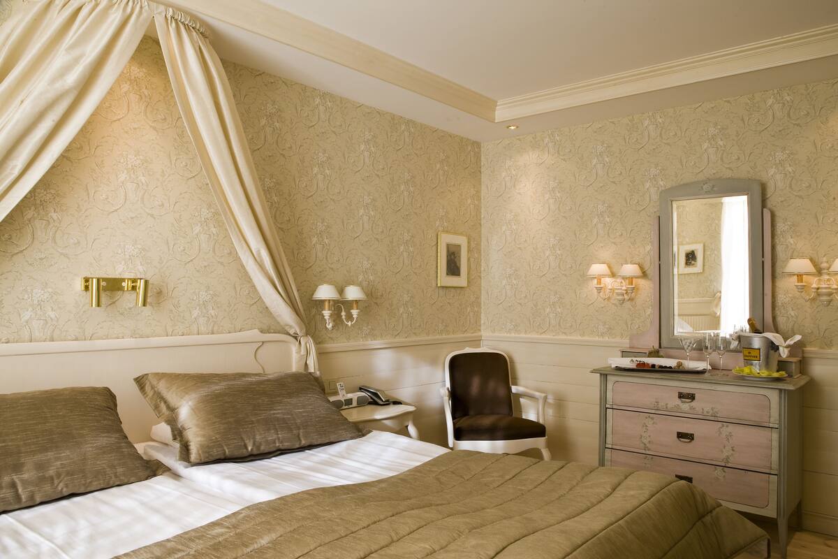 Ein Hotelzimmer mit einem Bett, einem Sessel, einem Schminktisch, einem Spiegel und Wandleuchten.