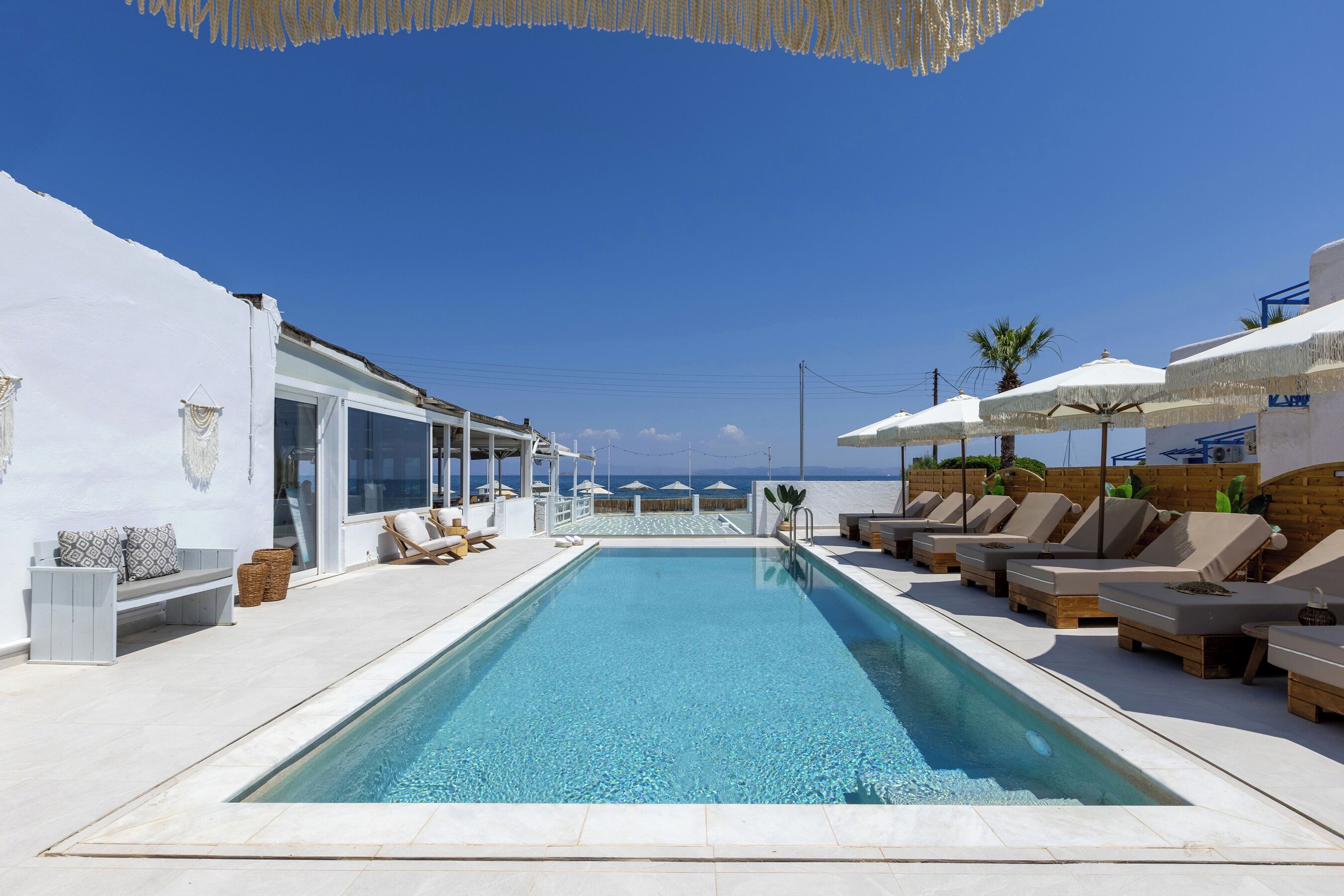 A pool area with lounge chairs and umbrellas, a clear blue sky, and a view of the sea.