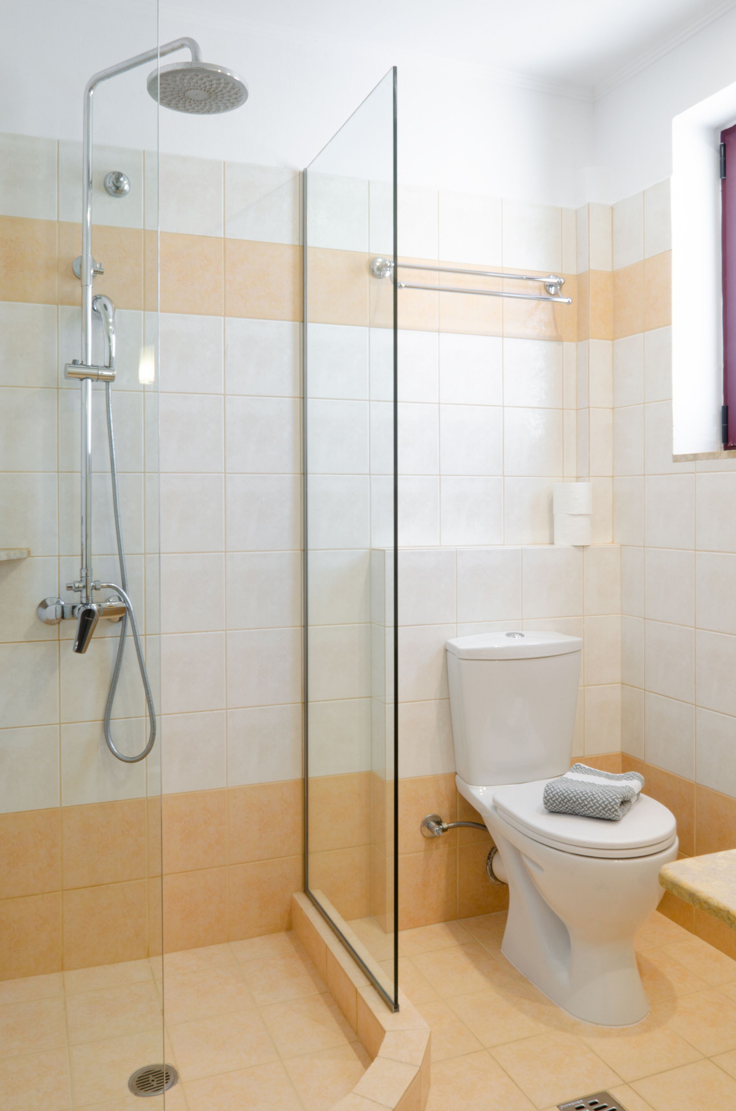 Une salle de bain moderne avec une douche à parois de verre, des toilettes blanches et un sol carrelé de couleur beige.