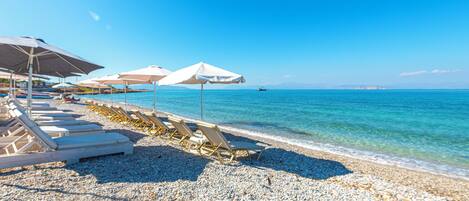 A beach with sun loungers and umbrellas, a pebble beach, and the sea.