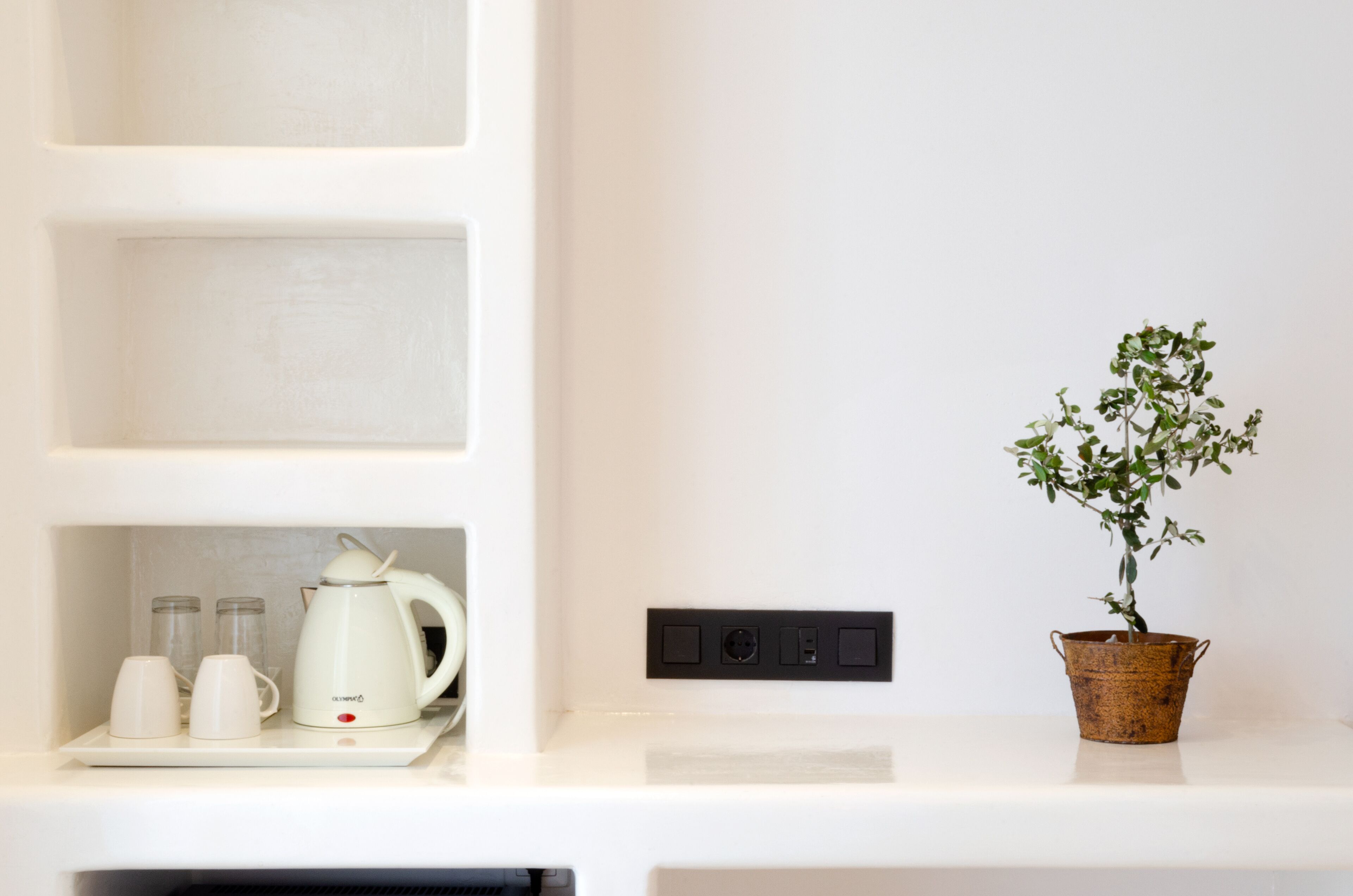 A white shelf with a coffee maker, two cups, and a potted plant.