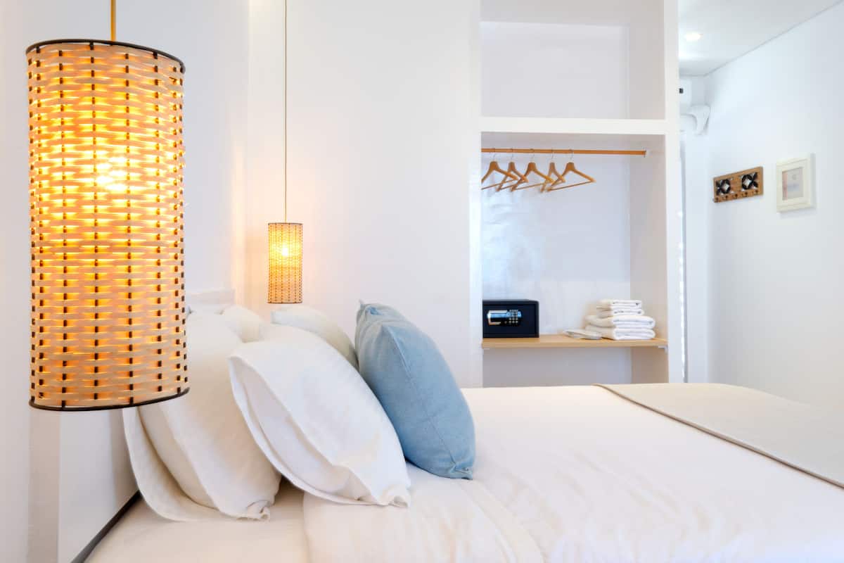 Une chambre moderne avec un lit, des oreillers, un luminaire suspendu, une armoire et une étagère avec des serviettes.