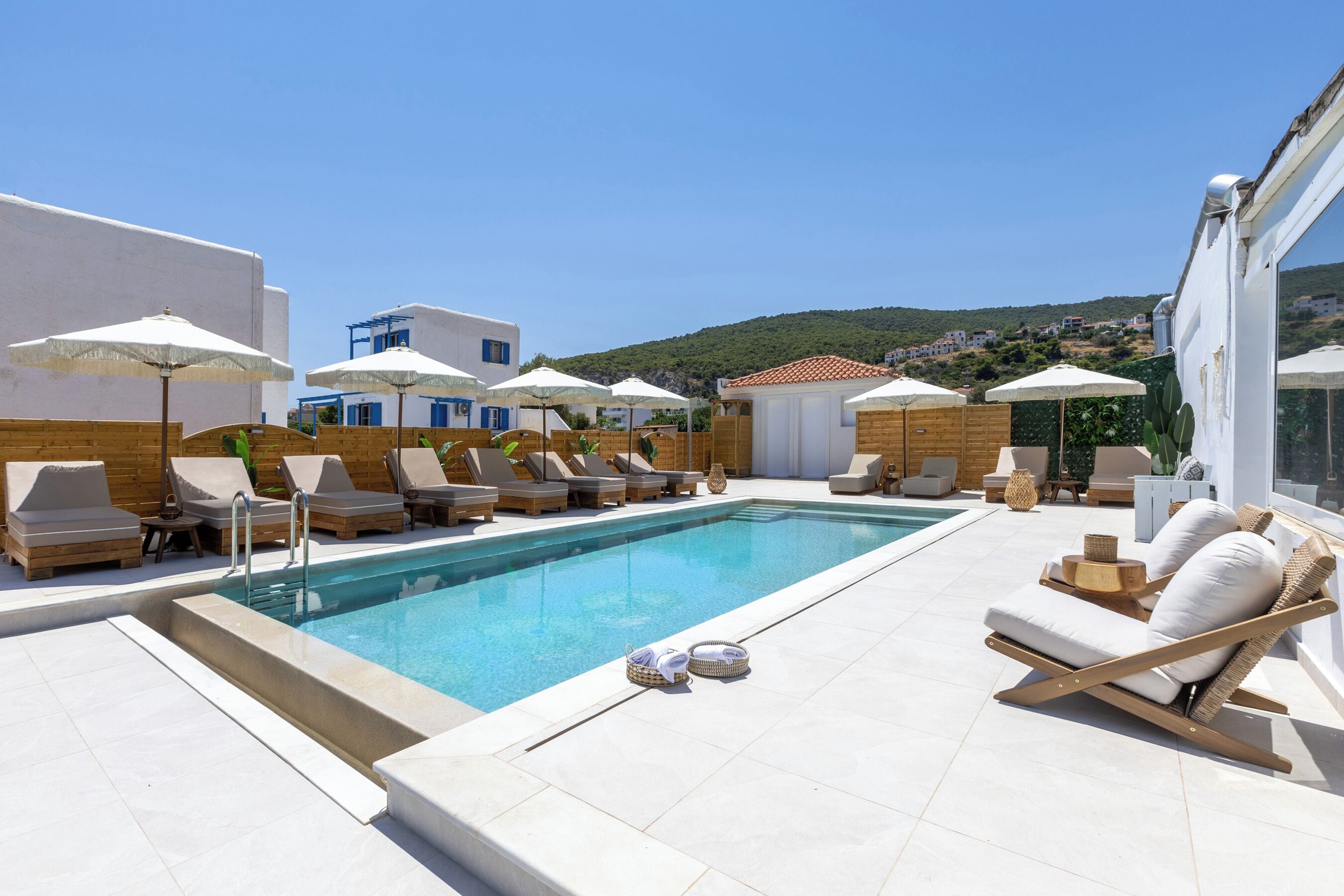 Zona junto a la piscina con sillones de descanso, sombrillas y una vista despejada de una colina al fondo.