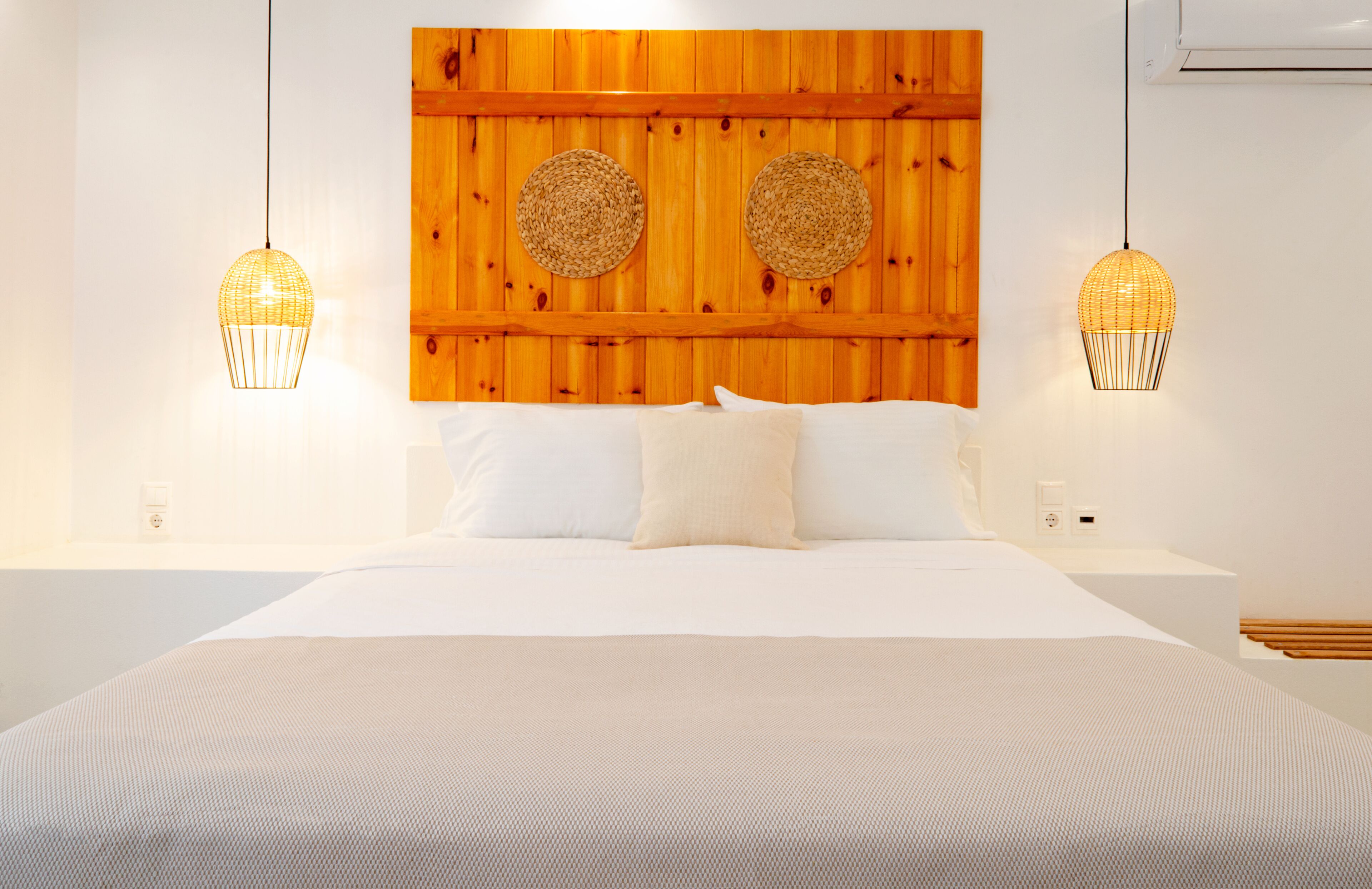 A bed with white linens, two woven lamps, and a wooden headboard with circular wall decorations.