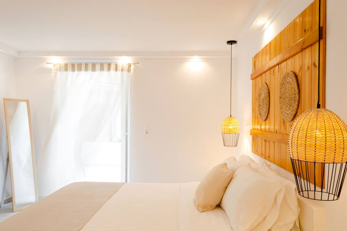 Une chambre à coucher comprenant un lit, un miroir, une fenêtre avec des rideaux et deux lampes fixées au mur.