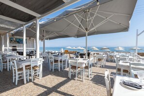 An outdoor dining area with white tables and chairs, umbrellas, and a view of the sea. - Laza Beach Inn (Agistri)