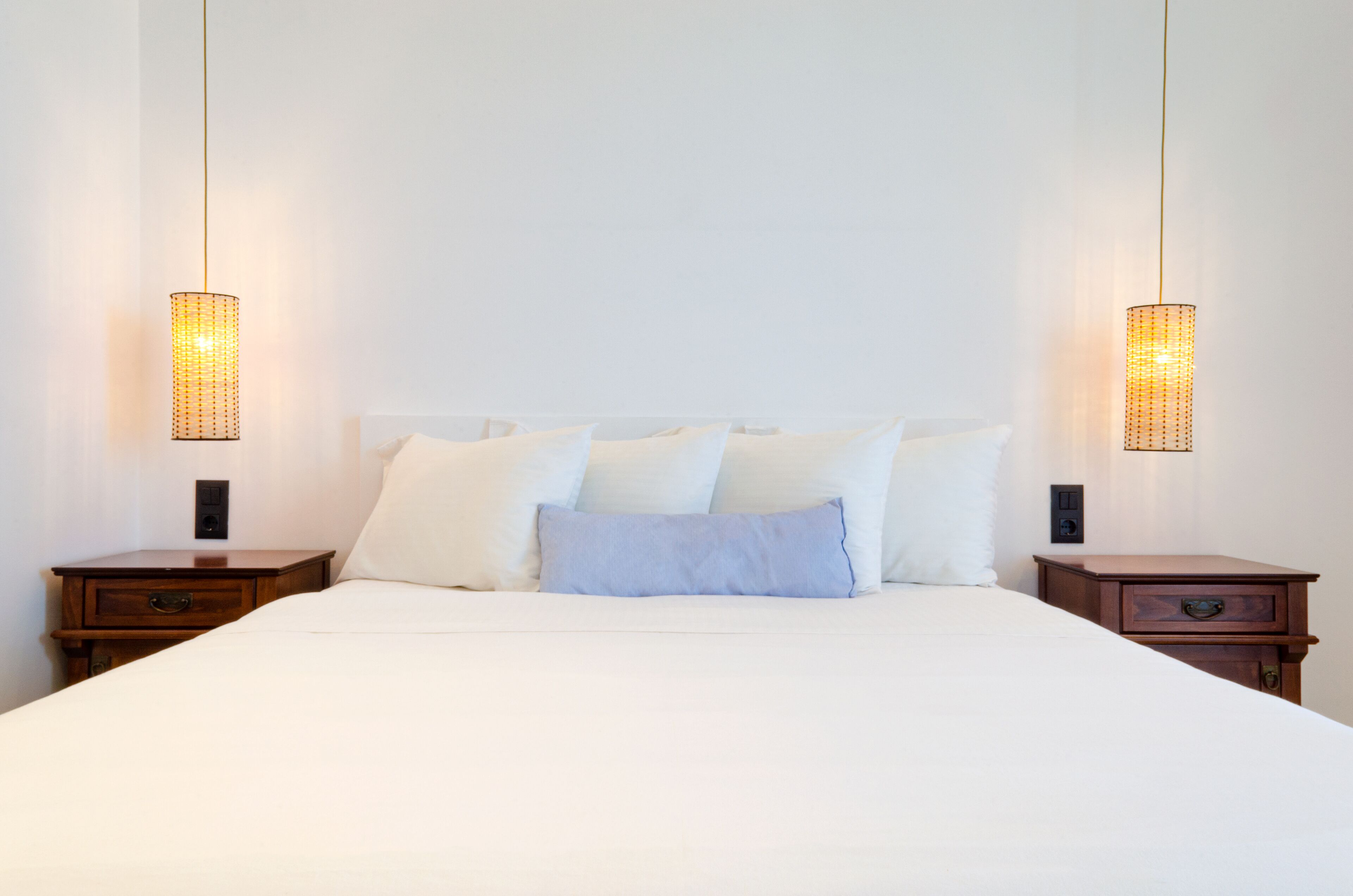 A neatly made bed with white linens and multiple pillows, flanked by two wooden nightstands with lamps.