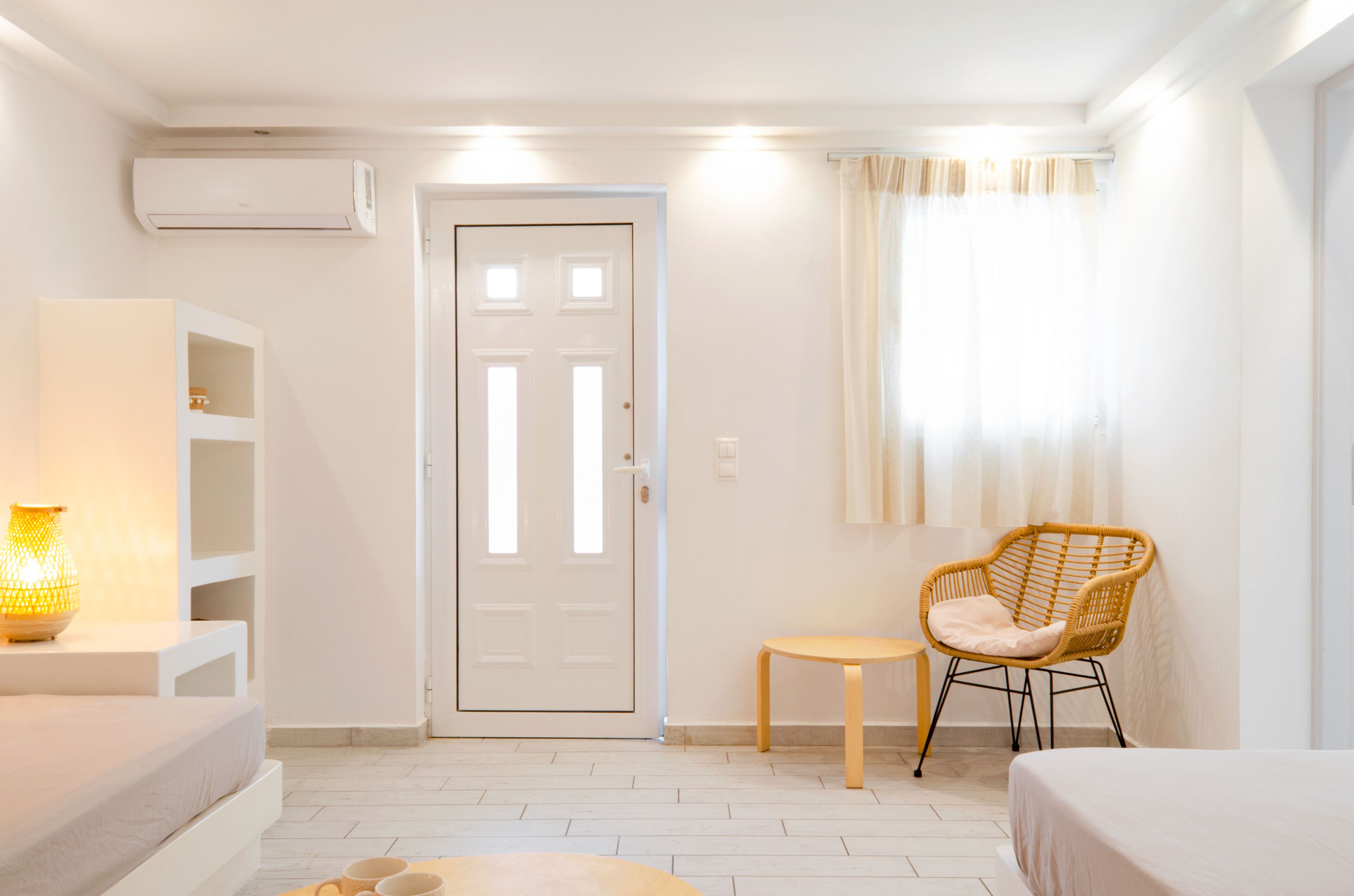 A modern, well-lit room with a bed, a small table, a wicker chair, and a shelf unit.