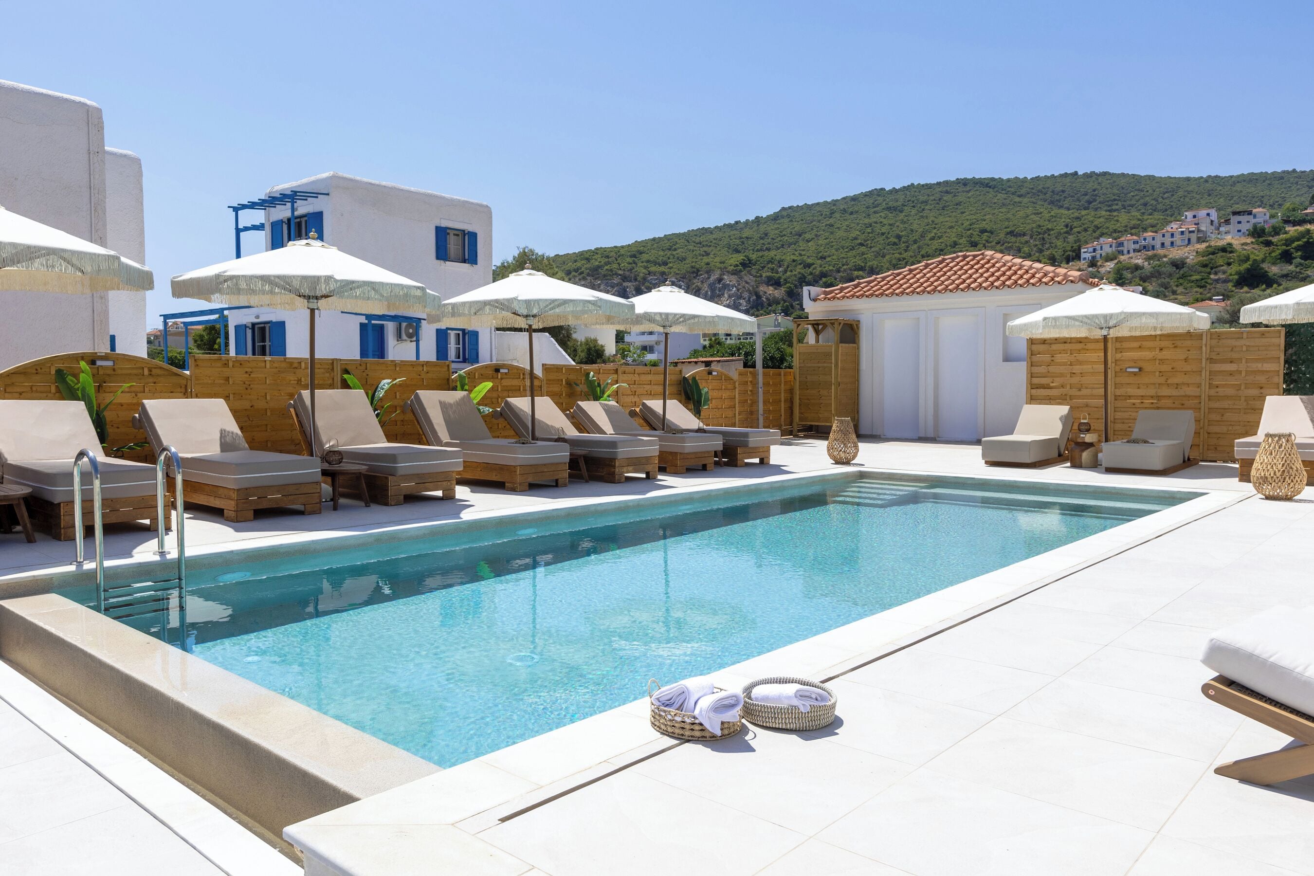 A poolside area with lounge chairs and umbrellas, a clear pool, and a view of a hillside.
