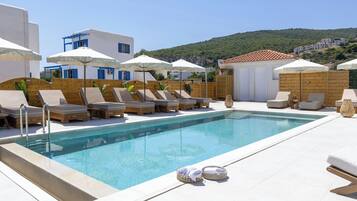 A poolside area with lounge chairs and umbrellas, a clear pool, and a view of a hillside.