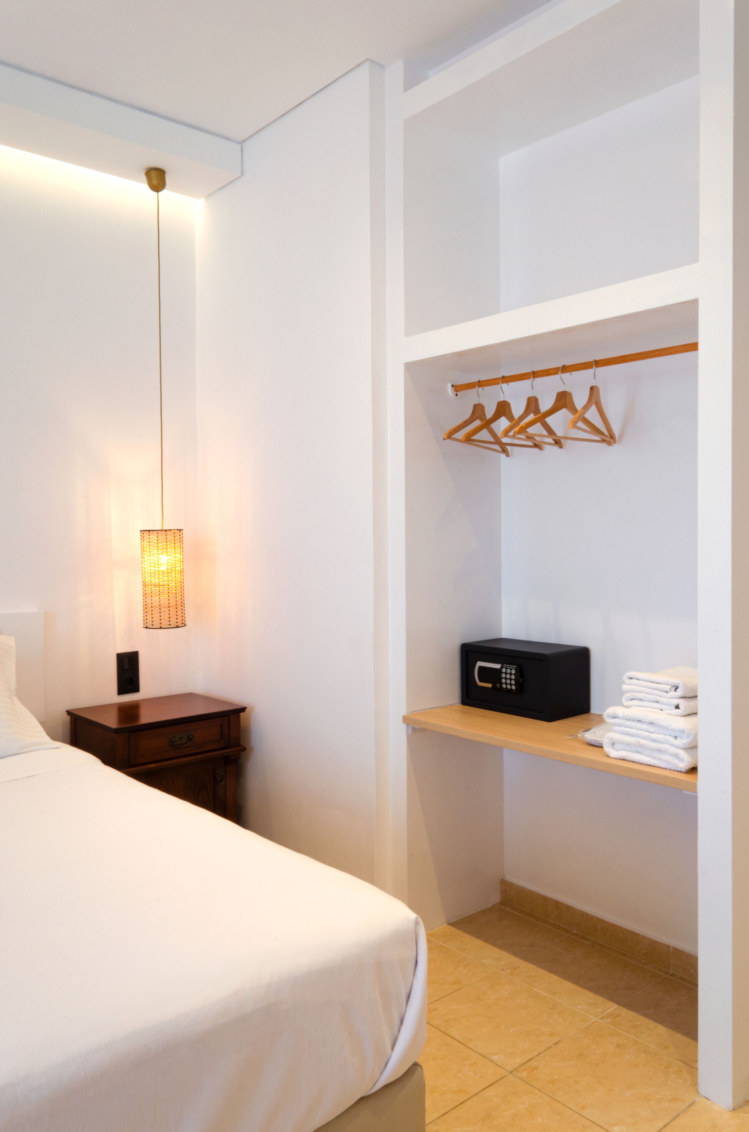 A hotel room with a bed, a bedside table with a lamp, a shelf with hangers, and a microwave.