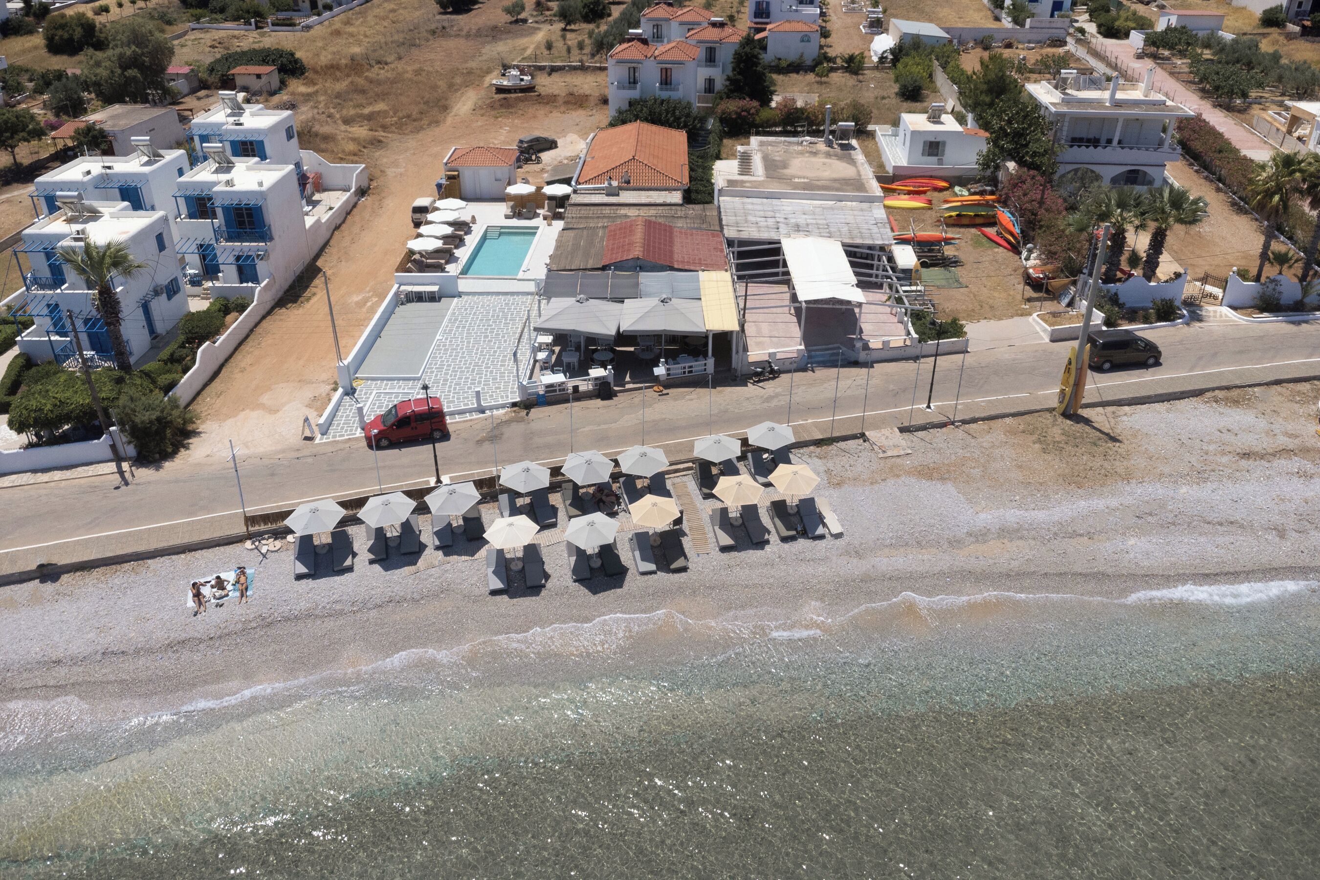 An aerial view of a coastal hotel with a swimming pool, beach umbrellas, and lounge chairs.