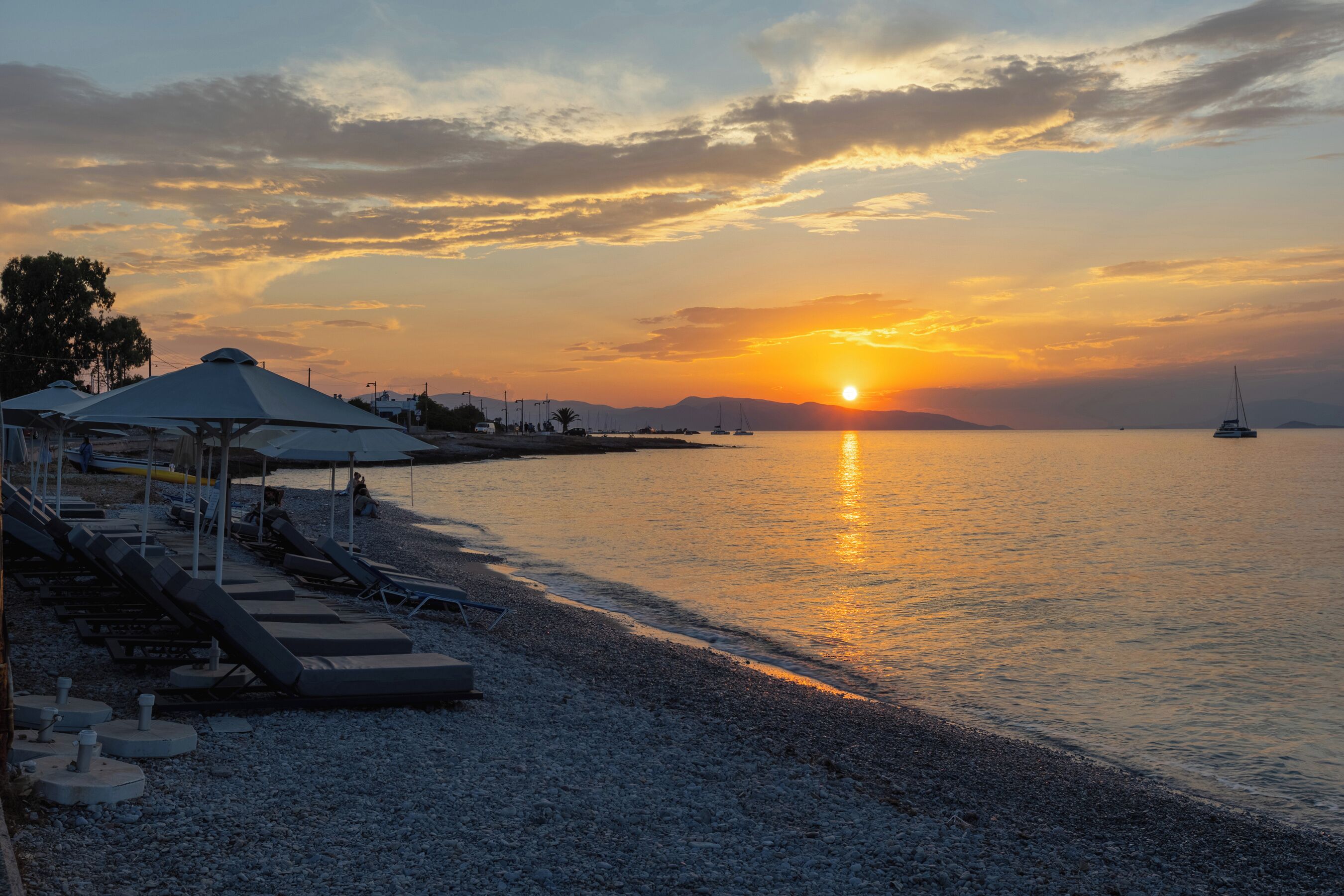 Ein Strand mit Liegestühlen und Sonnenschirmen, ruhiges Meer und ein Sonnenuntergang.