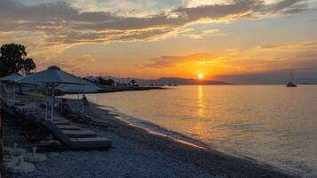 Ein Strand mit Liegestühlen und Sonnenschirmen, ruhiges Meer und ein Sonnenuntergang.