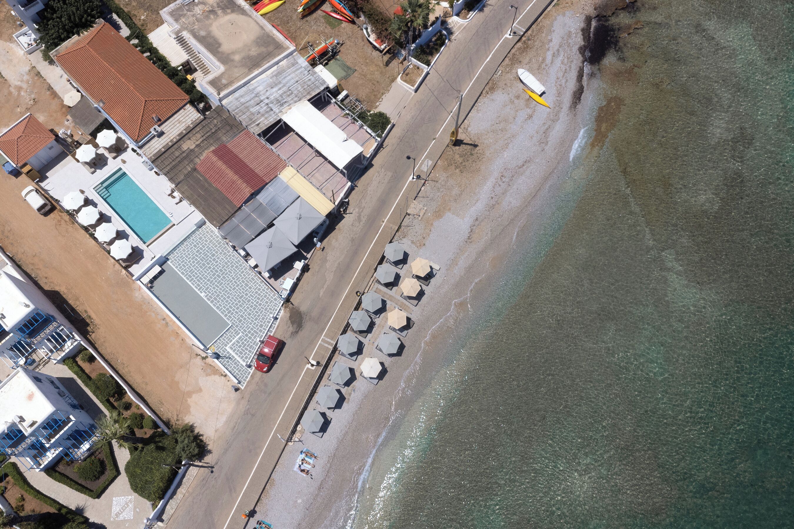 Eine Vogelperspektive auf ein Küstenanwesen mit Schwimmbad, Strandliegen und einer Straße, die zum Strand führt.