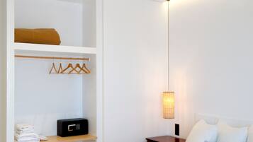 A bedroom with a large bed, wooden beams on the ceiling, a bedside table, a hanging light fixture, and a built-in wardrobe with a hanging rack.