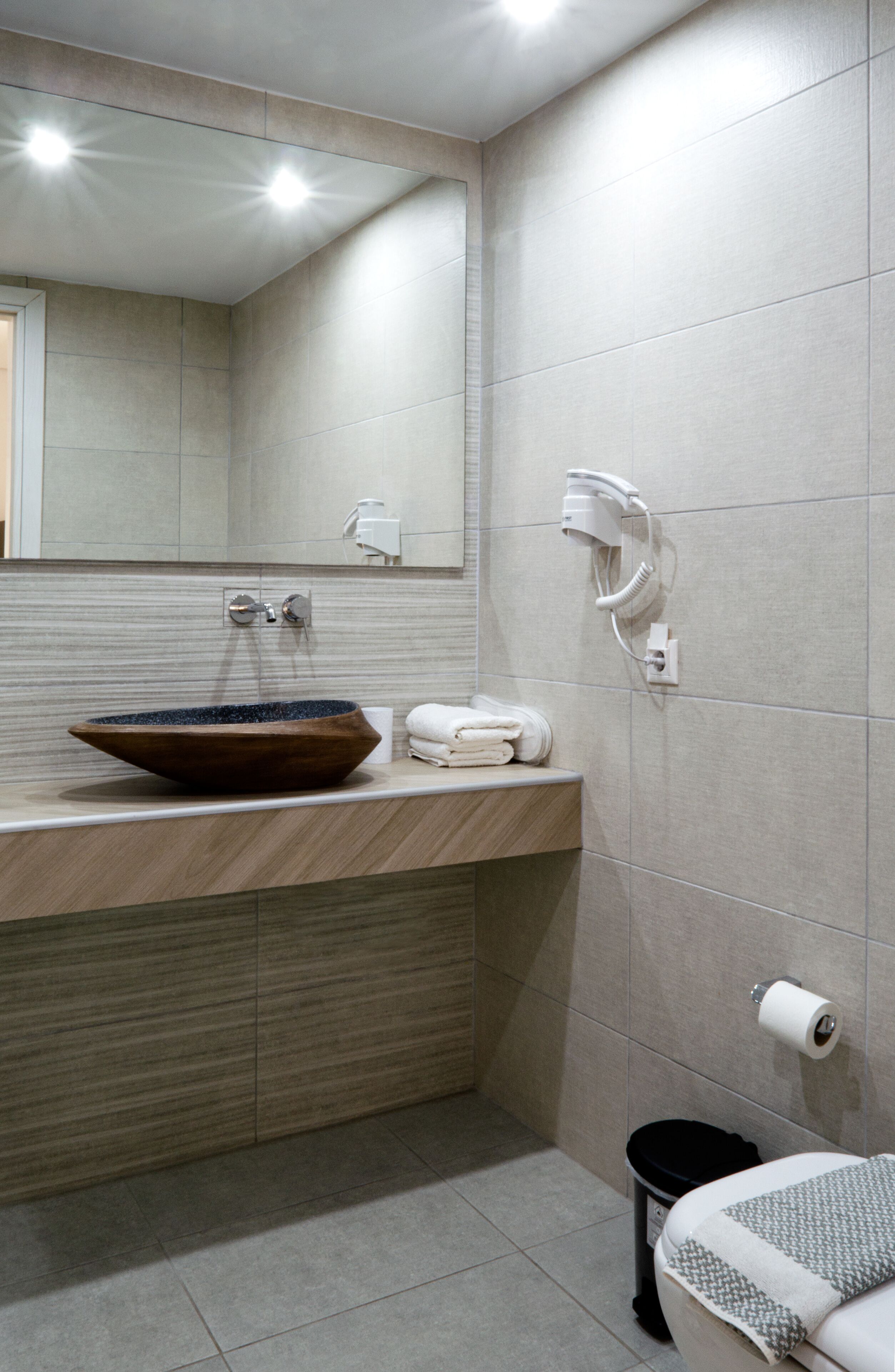 A modern bathroom with a wooden vanity, a large mirror, a hairdryer, and a toilet.