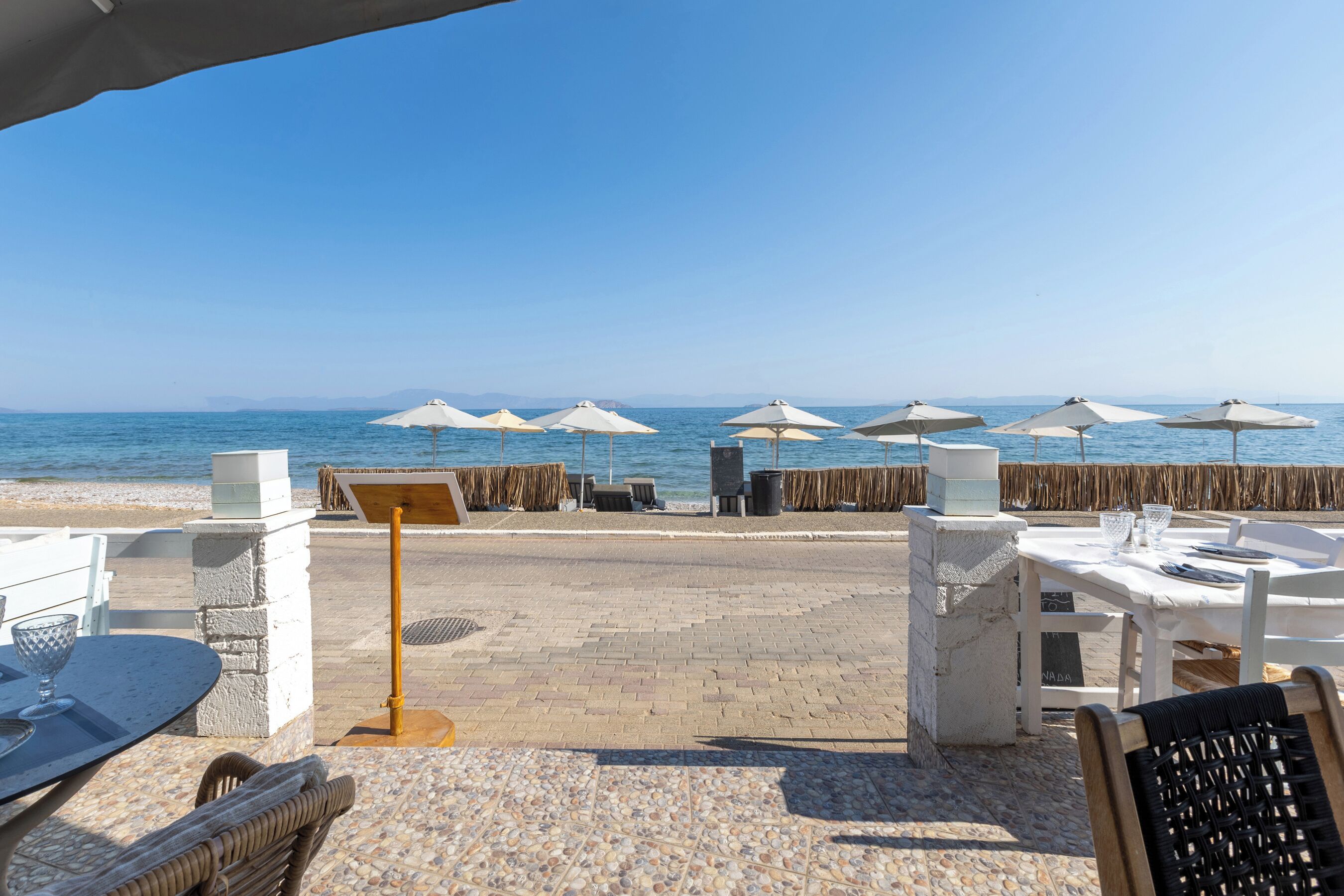 An outdoor seating area with tables and chairs, umbrellas, and a view of the sea.