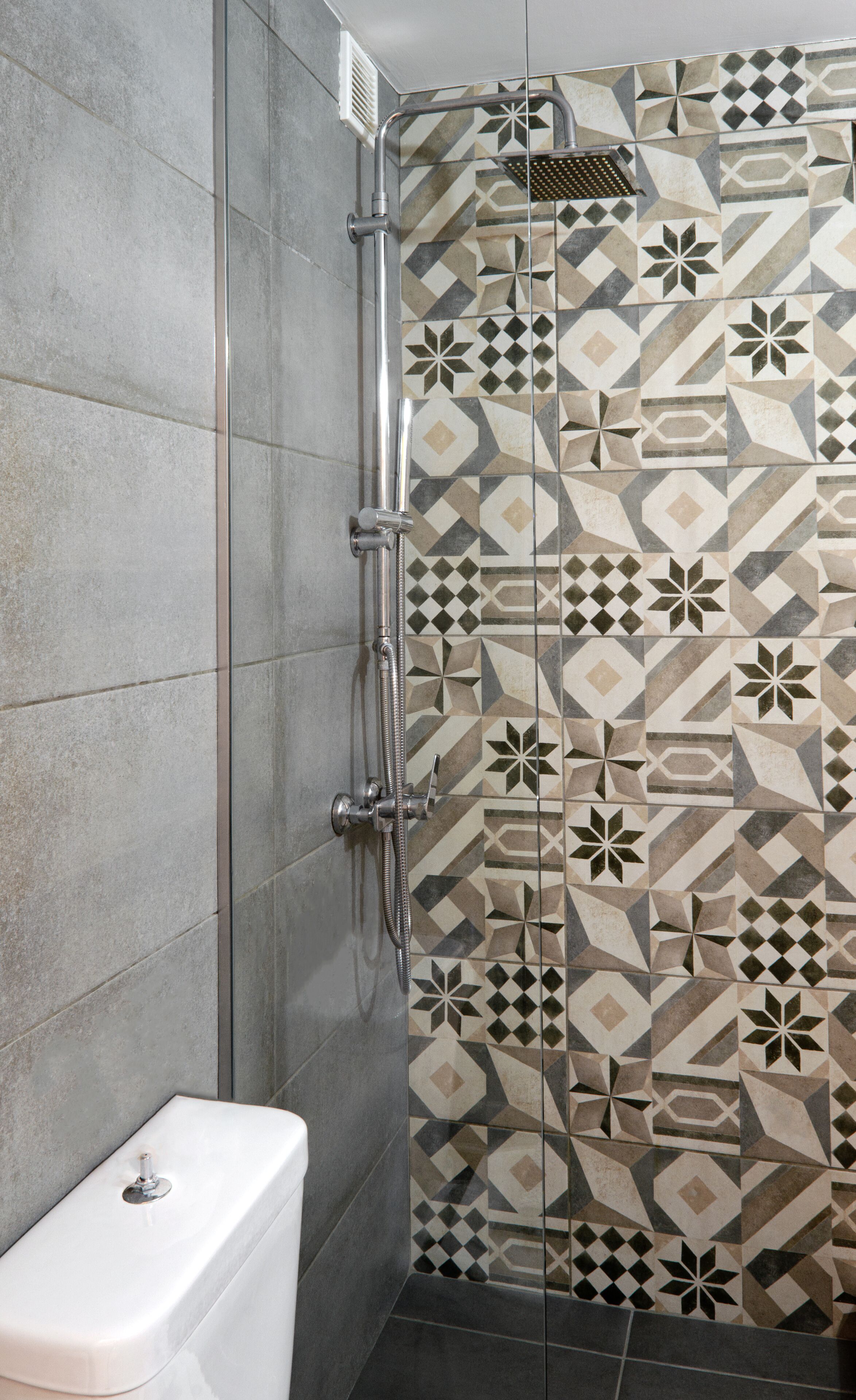 A shower area with a geometric tile pattern on the wall and a white toilet.