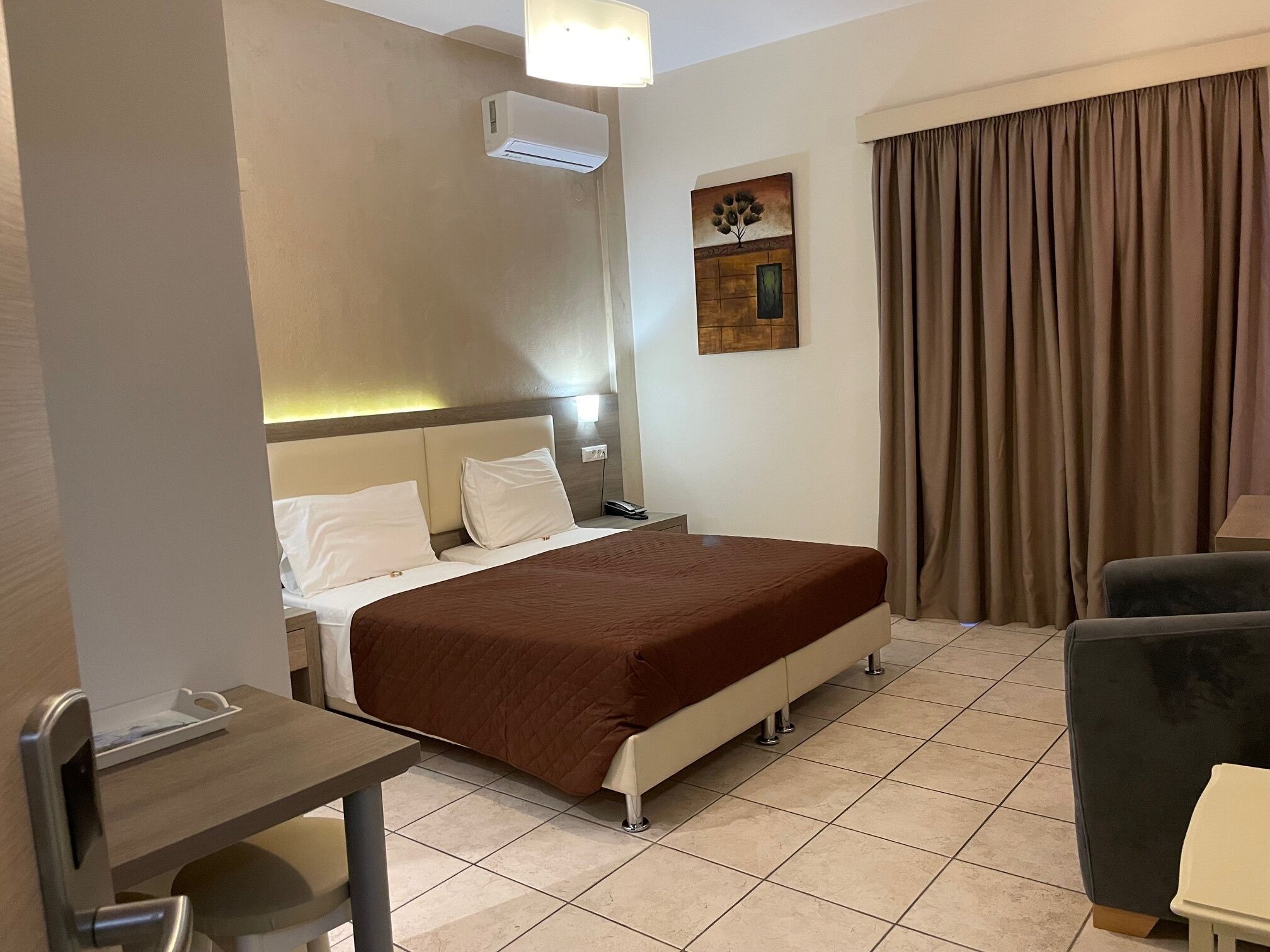 A hotel room with a bed, bedside table, chair, and a painting on the wall.