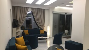 A modern living room with dark blue sofas, yellow cushions, a glass coffee table, and a sliding glass door leading to a balcony. - Voula Hotel (Hersonissos)