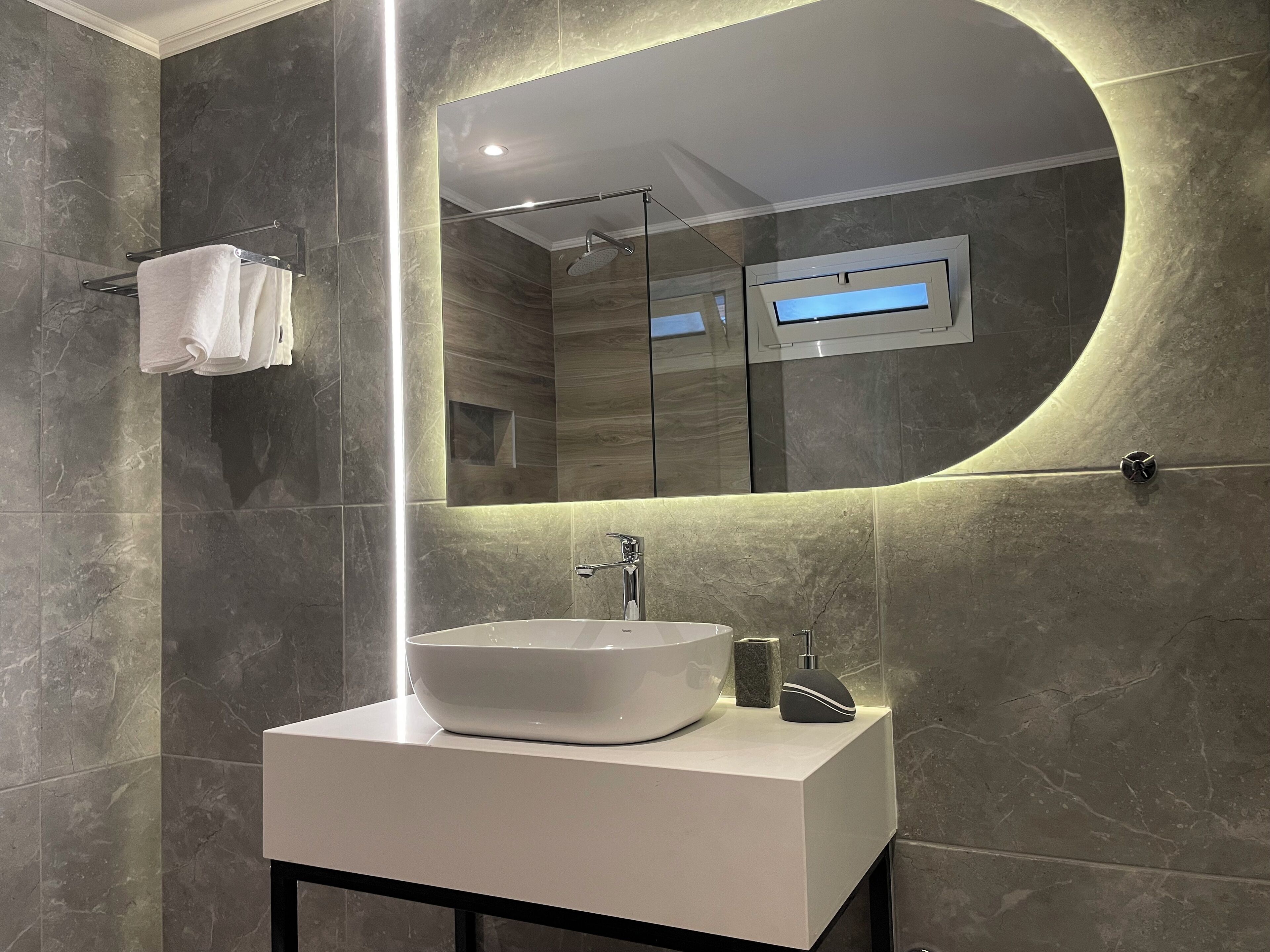 A modern bathroom with a large oval mirror, a white sink, and a handheld showerhead.