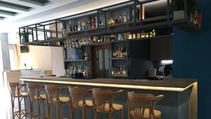 A bar area with a long counter and multiple stools, shelves with bottles, and a television screen. - Voula Hotel (Hersonissos)