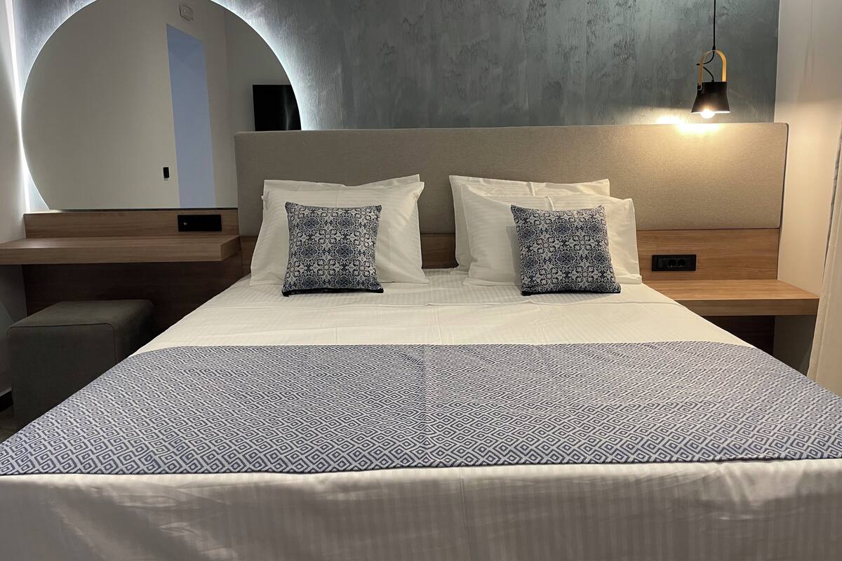 A modern hotel room with a large bed, two nightstands, a circular mirror, and a hanging light fixture.