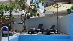 A swimming pool with two lounge chairs and a tree. - Voula Hotel (Hersonissos)