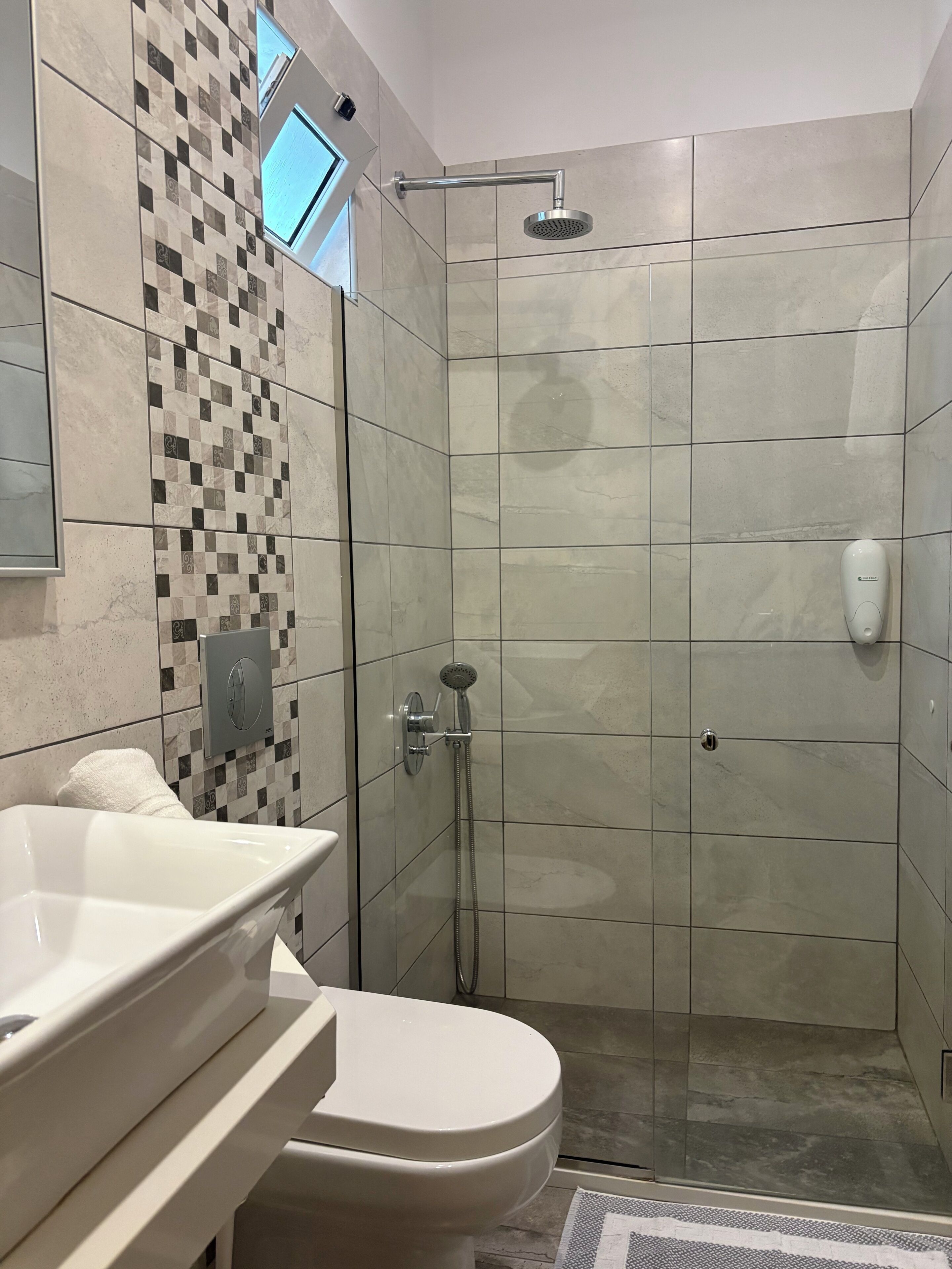 Un baño moderno con ducha separada por vidrio, inodoro y lavamanos con espejo.
