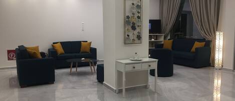 A modern living room with a dark blue sofa set, a white side table, and a decorative wall piece.