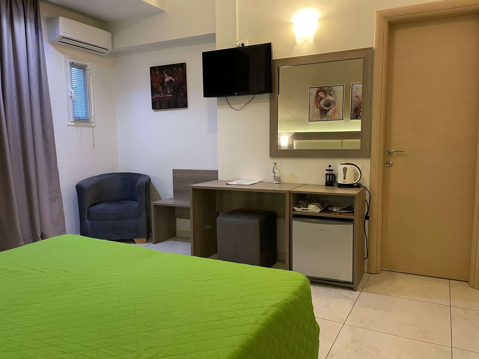 Habitación de hotel con cama, escritorio, silla, televisor, espejo y puerta.